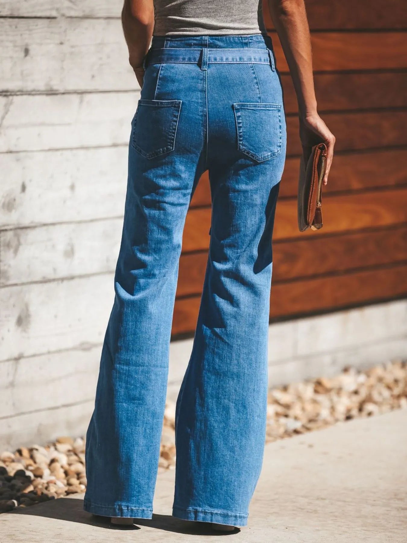 Person wearing blue jeans standing against a wooden wall.