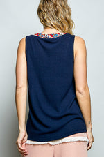 Person wearing a navy sleeveless top with floral patterned trim on a plain background