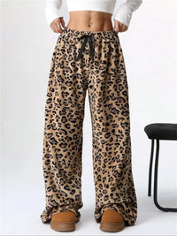 Leopard print pants worn with a white top and brown slippers on a white background