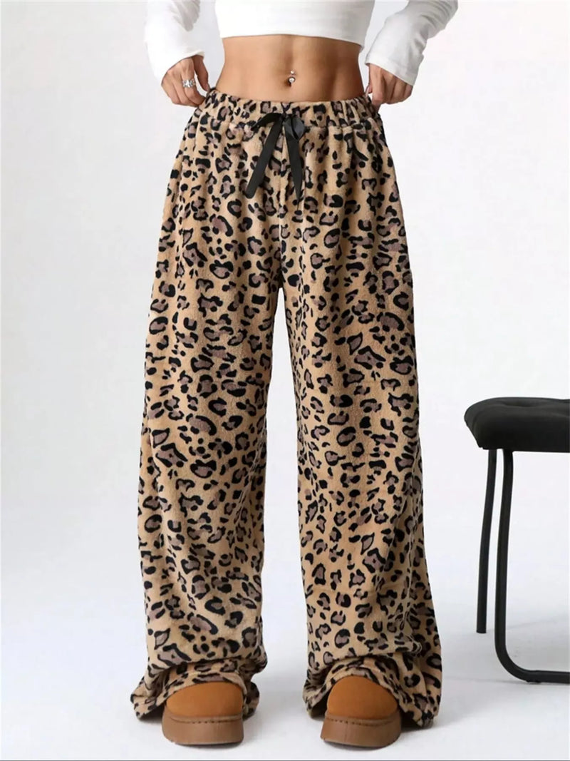 Leopard print pants worn with a white top and brown slippers on a white background