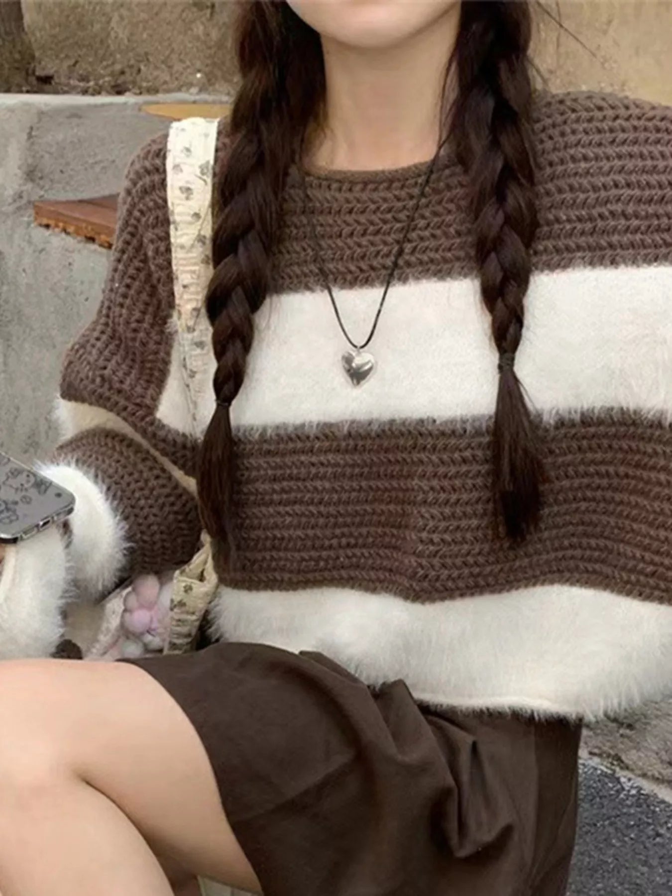 Person wearing a brown and white striped sweater sitting on a stone surface with a cat.