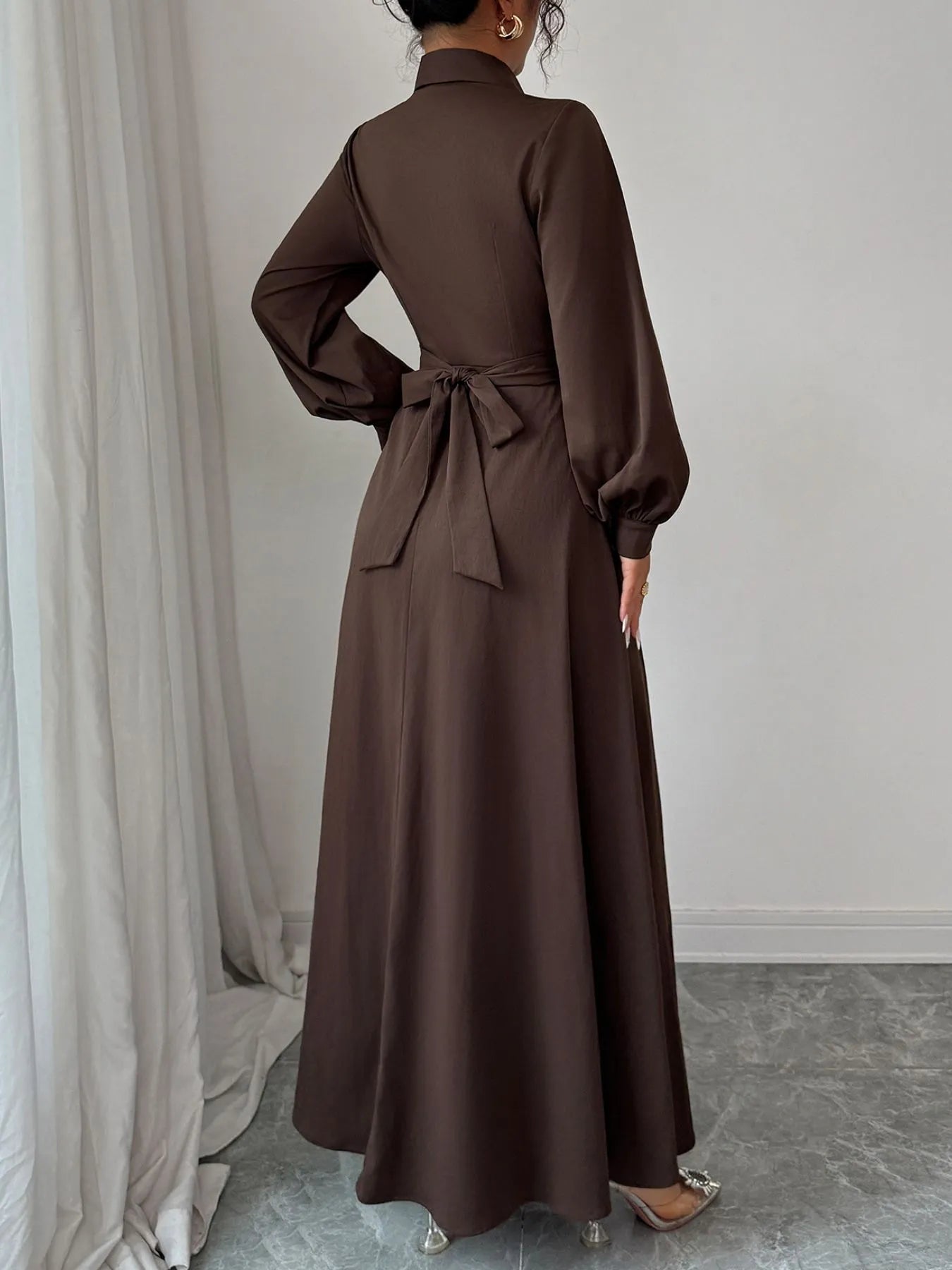 Brown long-sleeve dress with a belt worn by a person, standing against a neutral background.