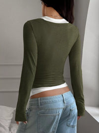 Person wearing a green long-sleeve top and blue jeans against a neutral background