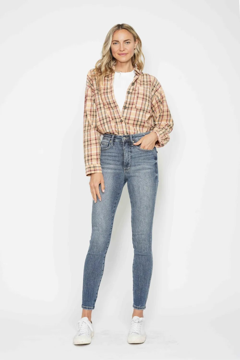 Woman wearing a plaid shirt and blue jeans against a white background