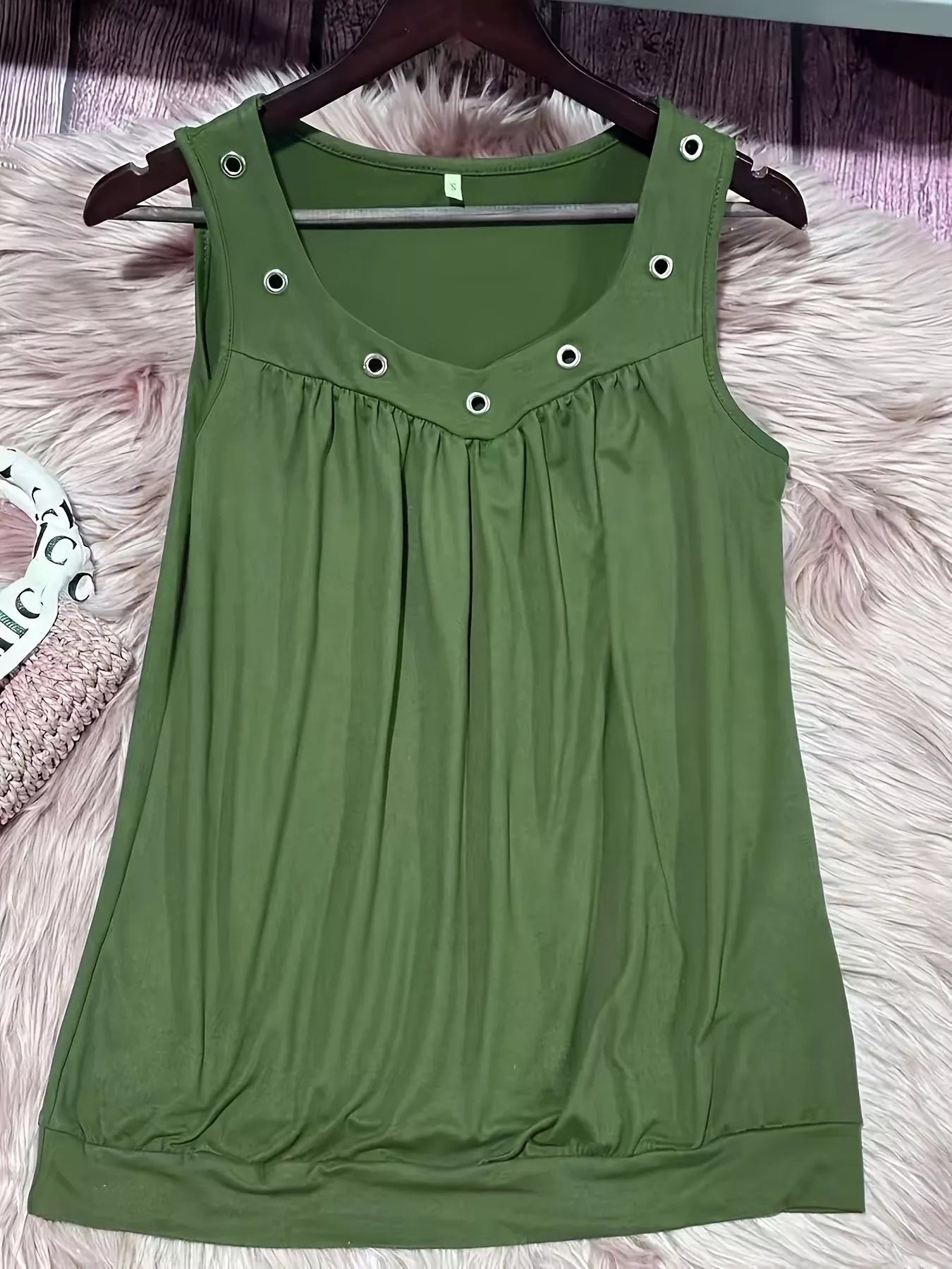 Green sleeveless dress with button details on a hanger against a fluffy pink surface.