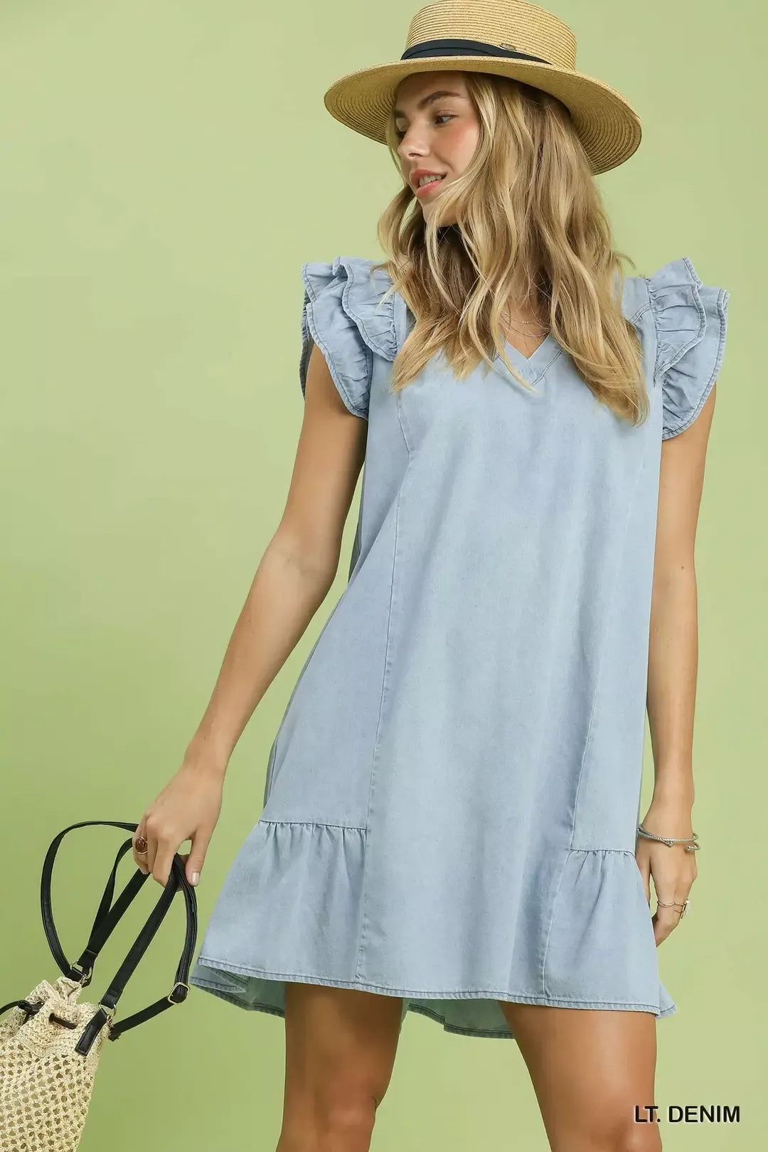 Woman wearing a light blue denim dress with ruffled sleeves against a green background