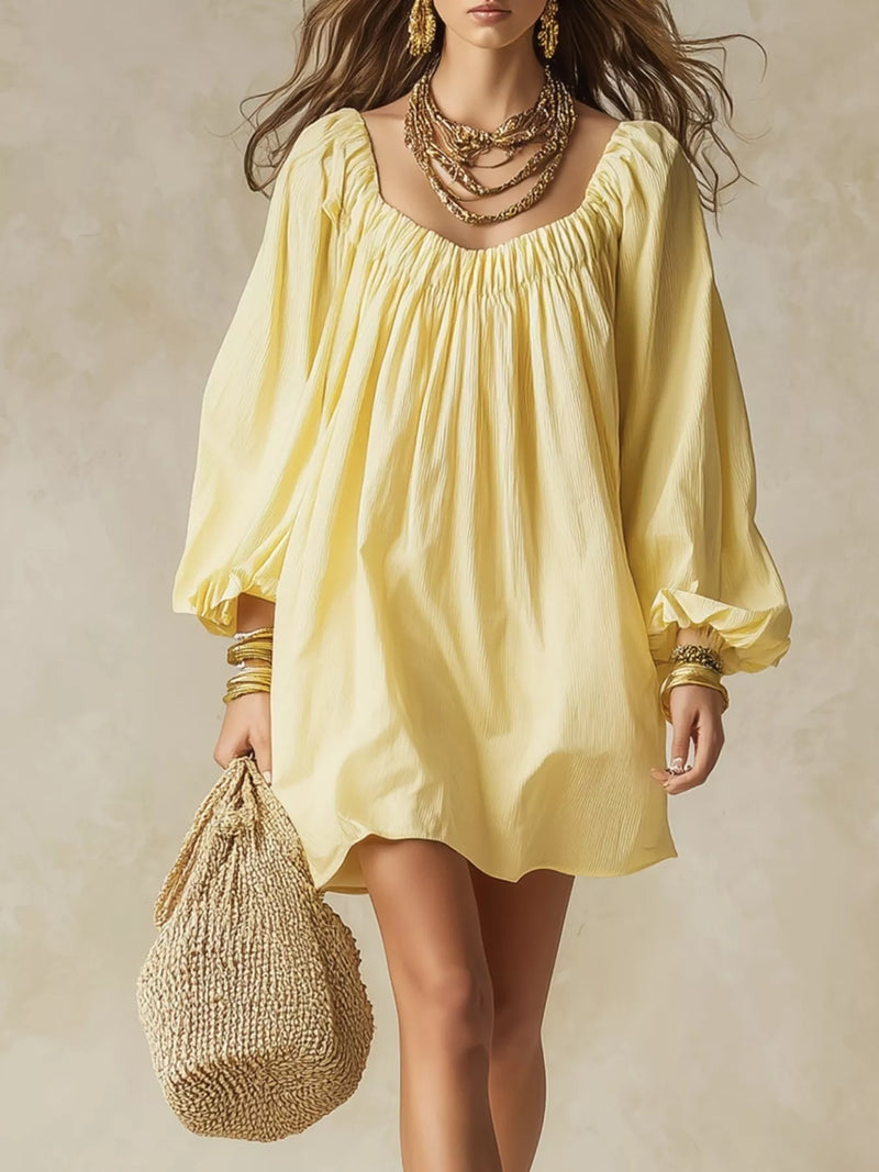 A woman wearing a pale yellow puff-sleeve mini dress with a square neckline and gathered waist, styled with layered gold necklaces, bracelets, and a woven straw bag against a textured beige background.