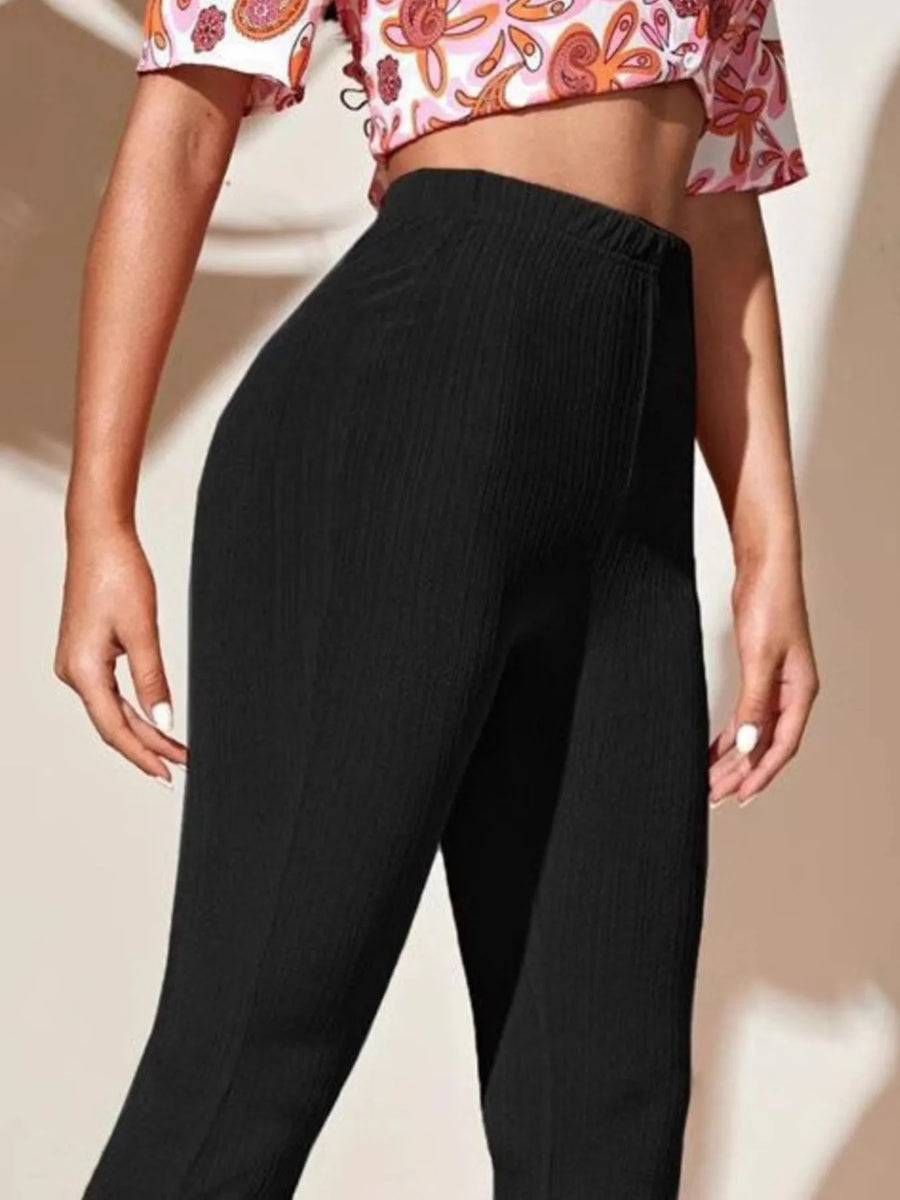 Person wearing black pants and a patterned top on a beige background