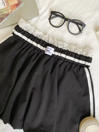 Black shorts with lace trim on a white surface with glasses and a magazine.