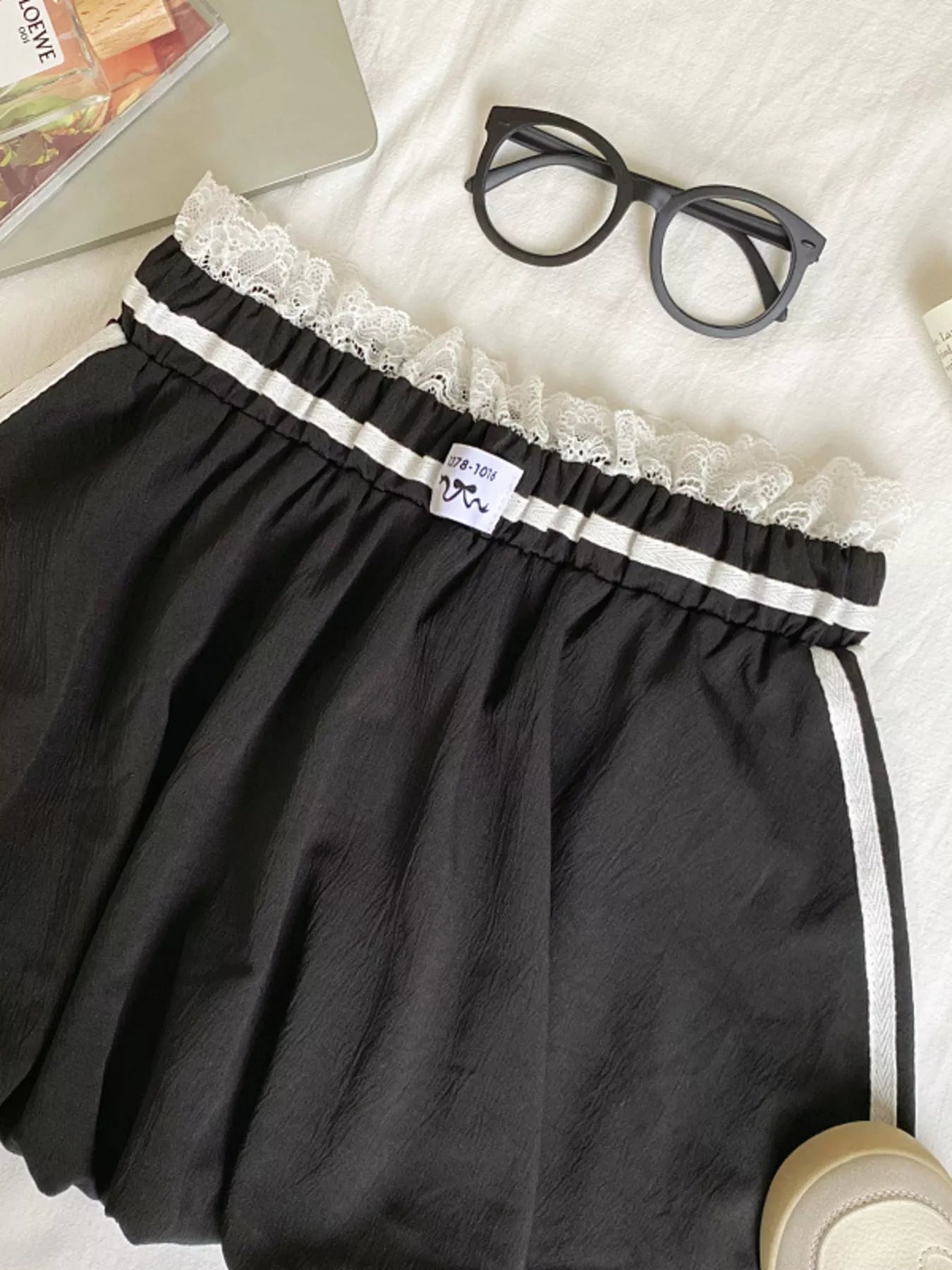 Black shorts with lace trim on a white surface with glasses and a magazine.
