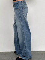 A person wearing wide-leg light blue denim jeans, shown from the waist down against a plain light gray wall and concrete floor.