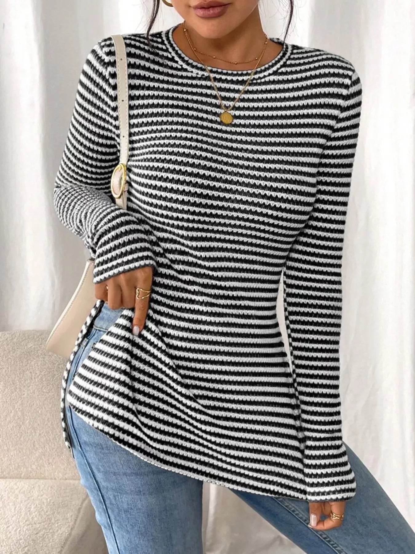 Person wearing a black and white striped sweater with blue jeans against a neutral background