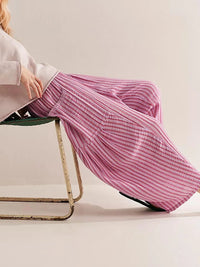 Person wearing pink striped pants sitting on a chair with a plain background