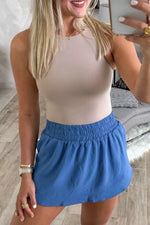 Woman taking a mirror selfie wearing a beige tank top and blue shorts.