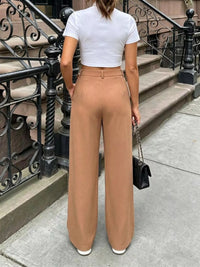 Person wearing a white crop top and tan wide-leg pants standing on a city street.