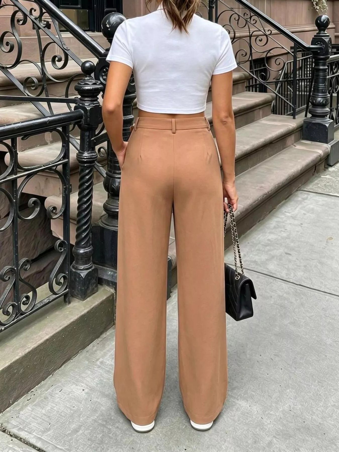 Person wearing a white crop top and tan wide-leg pants standing on a city street.