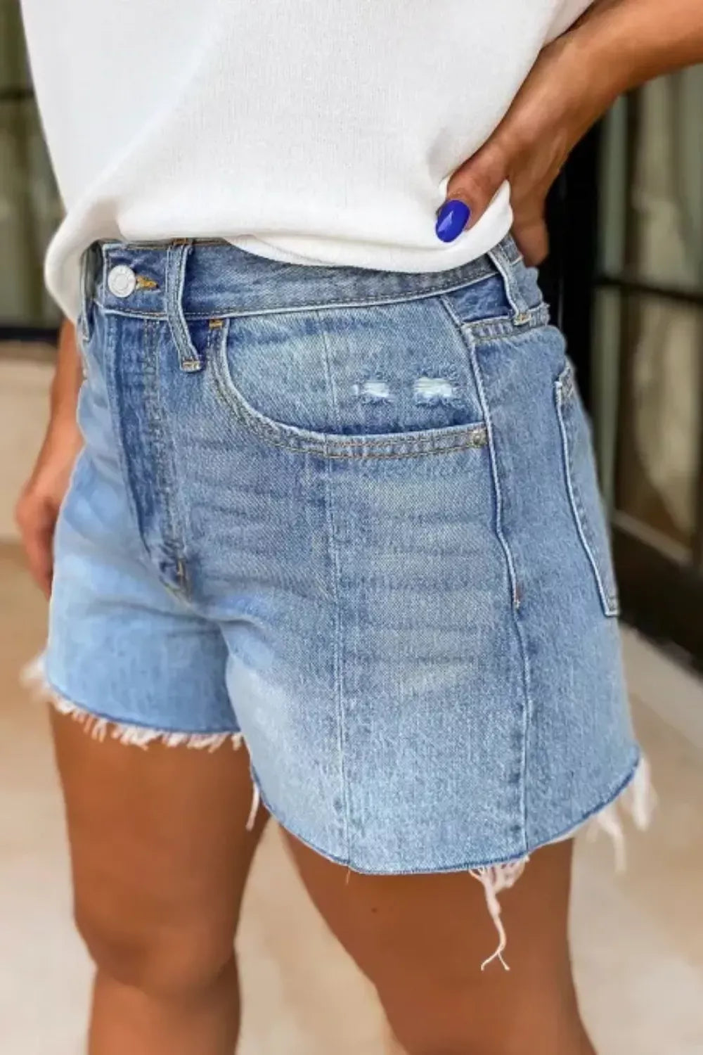 Person wearing light blue denim shorts with a white top indoors.