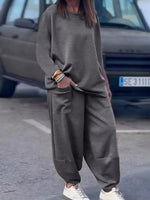 Person wearing a gray oversized sweater and pants with white sneakers on a street.