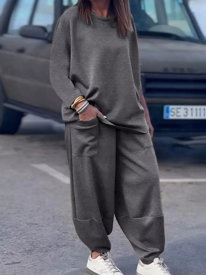 Person wearing a gray oversized sweater and pants with white sneakers on a street.