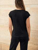 Person wearing a black top and pants against a beige stone wall.