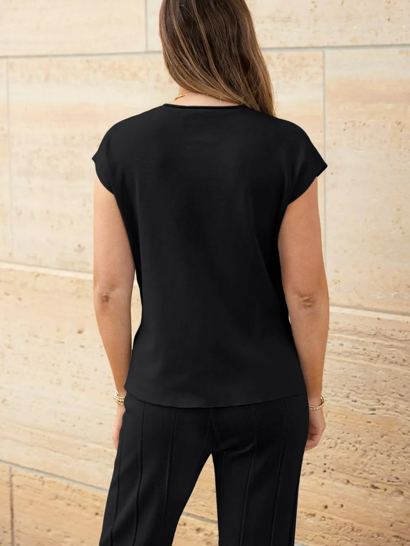 Person wearing a black top and pants against a beige stone wall.
