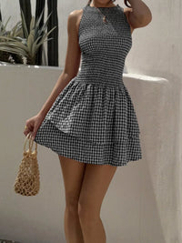 Woman wearing a black and white checkered dress holding a woven handbag against a neutral background.