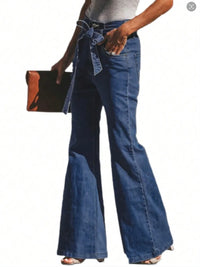 Person wearing blue bell-bottom jeans holding a black clutch on a white background