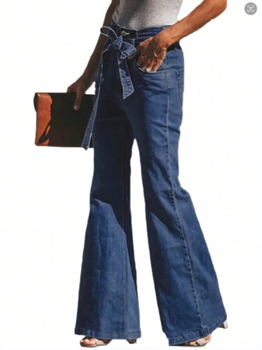 Person wearing blue bell-bottom jeans holding a black clutch on a white background