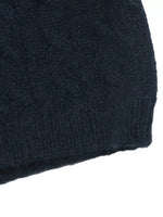 Close-up of a dark navy blue knit fabric, showing a textured cable-knit pattern and ribbed edge against a white background.