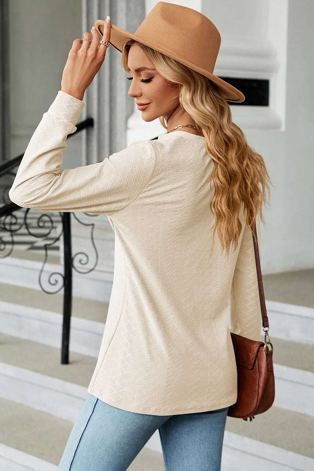 Woman wearing a beige sweater and tan hat, holding a brown handbag.