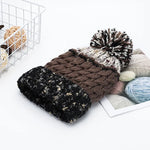Knitted hat with pom-pom on a white surface with yarn balls in the background