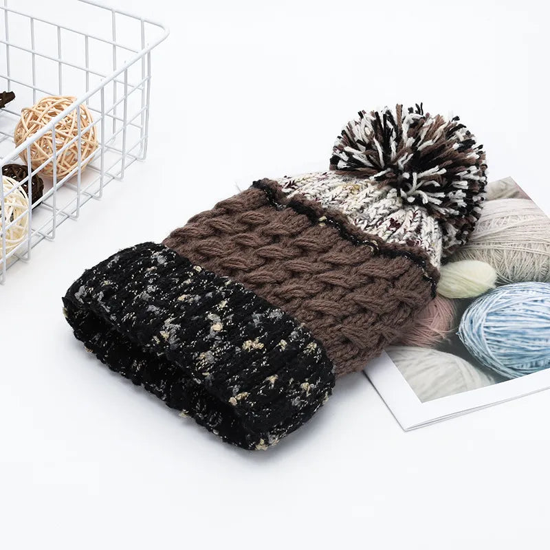 Knitted hat with pom-pom on a white surface with yarn balls in the background