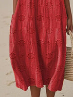 Red dress with textured pattern worn by a person on a beach.