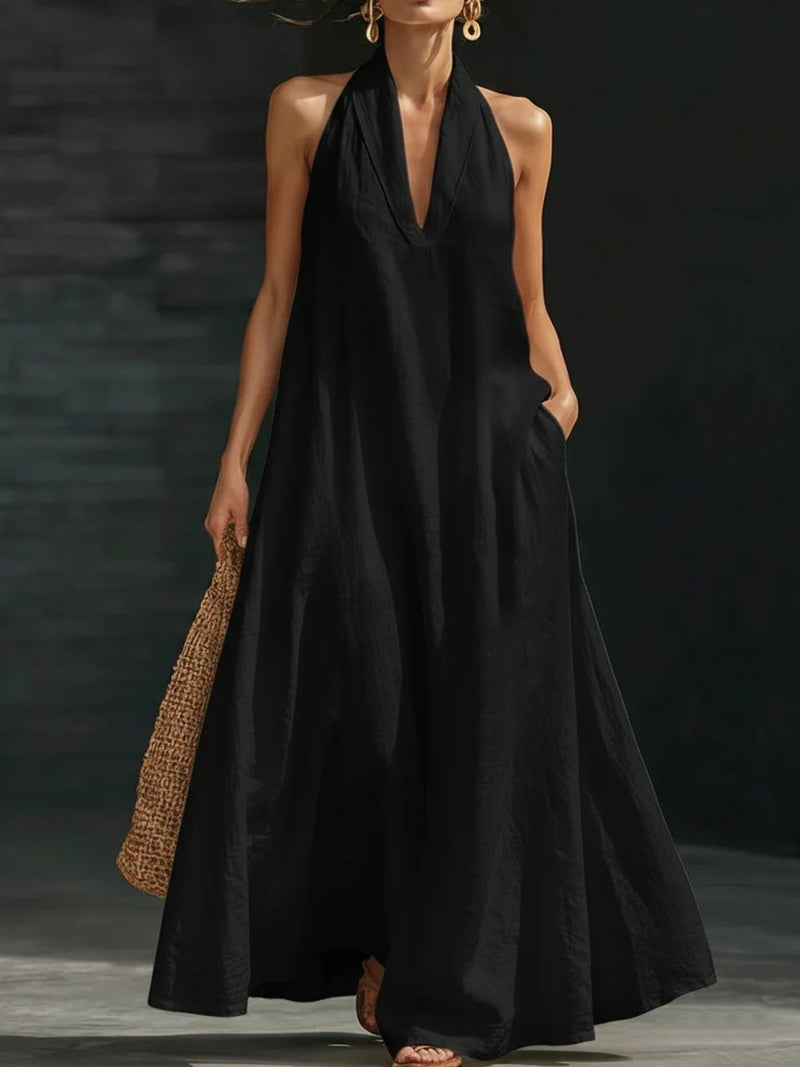 Woman wearing a black halter neck dress holding a woven bag against a dark background