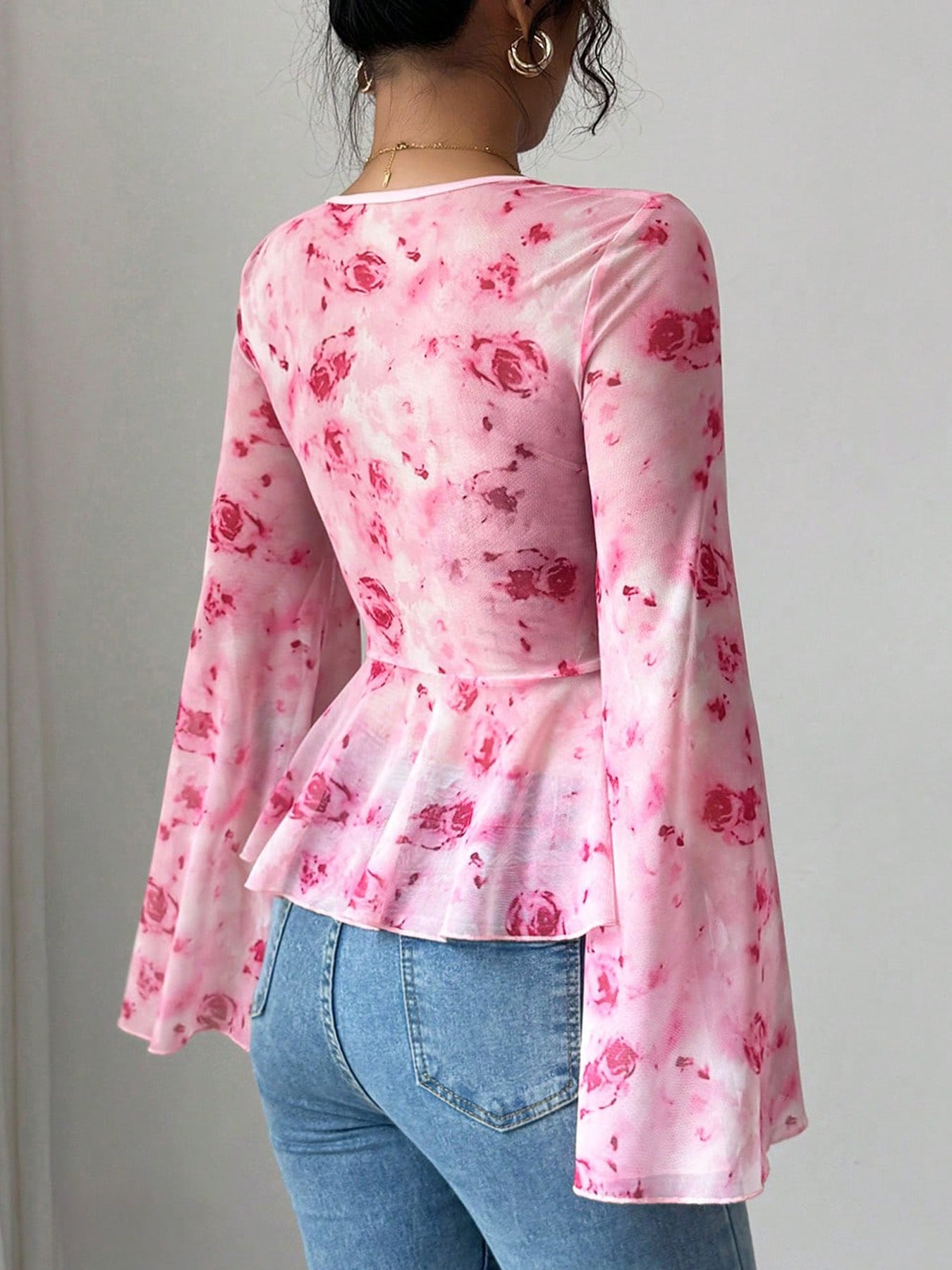 Person wearing a pink floral long-sleeve top and blue jeans against a plain background