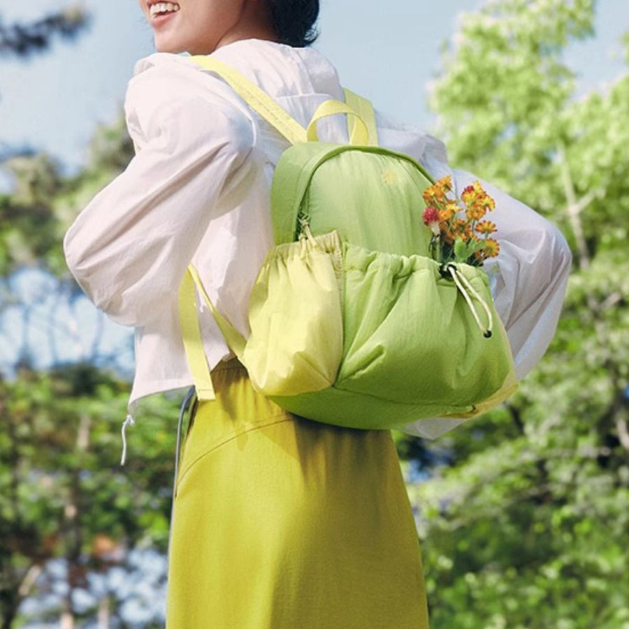 Person wearing a green backpack with flowers, standing outdoors with trees in the background