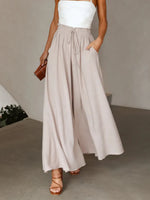 Woman wearing a white top and beige wide-leg pants against a neutral background