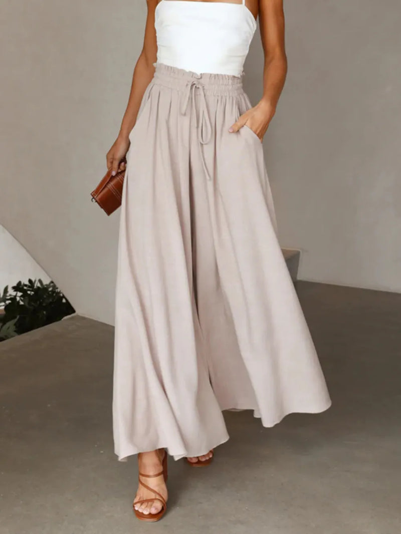 Woman wearing a white top and beige wide-leg pants against a neutral background