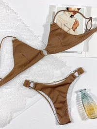 Brown bikini set on a white surface with a magazine and bottle in the background