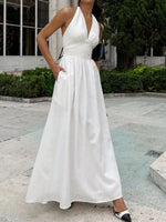 Woman wearing a white halter neck dress standing outdoors.
