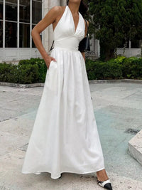 Woman wearing a white halter neck dress standing outdoors.