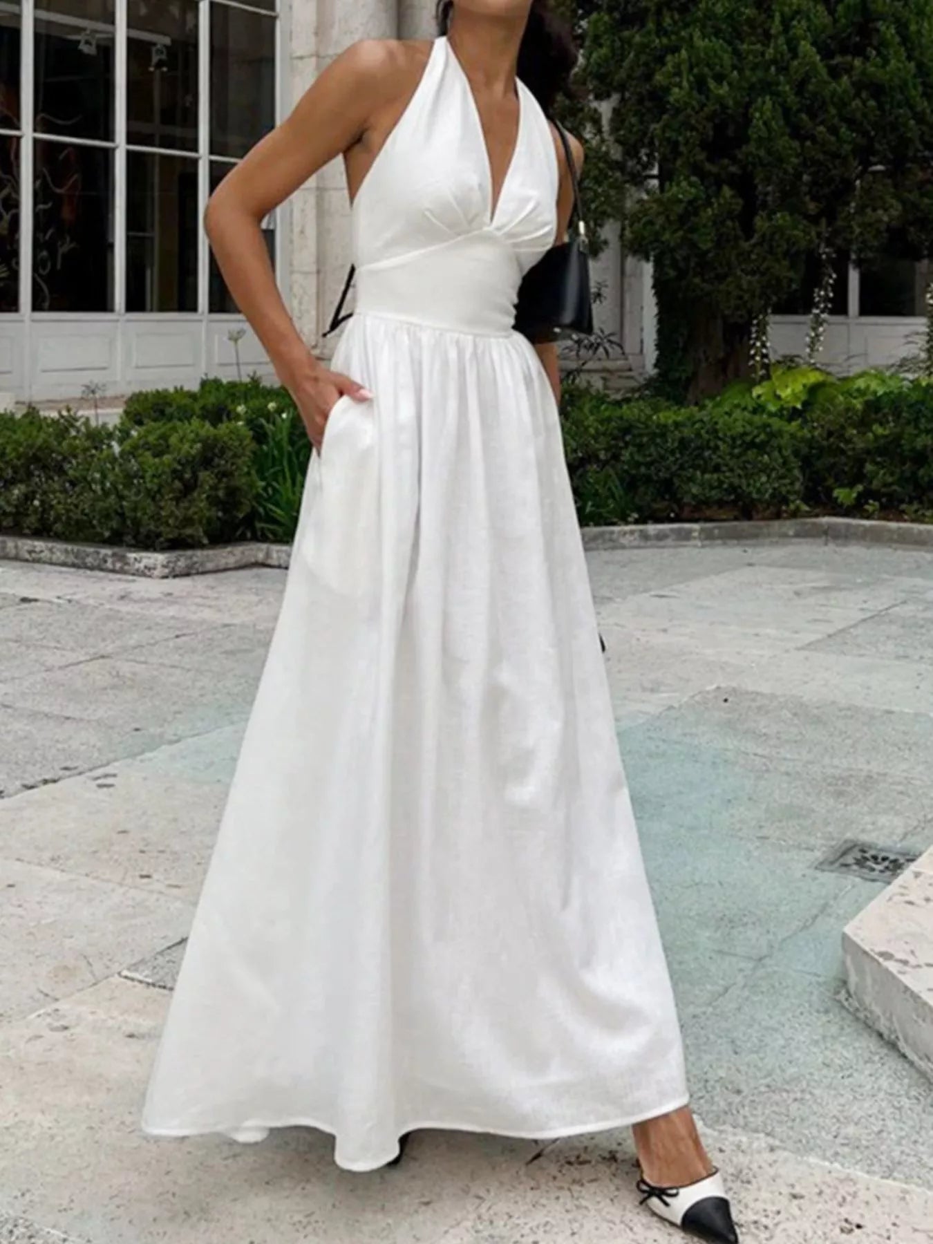 Woman wearing a white halter neck dress standing outdoors.