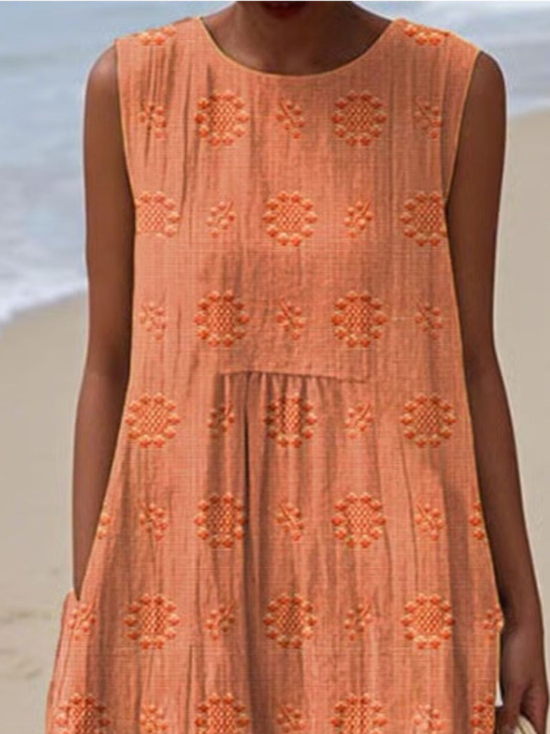 Person wearing an orange dress with floral patterns on a beach.