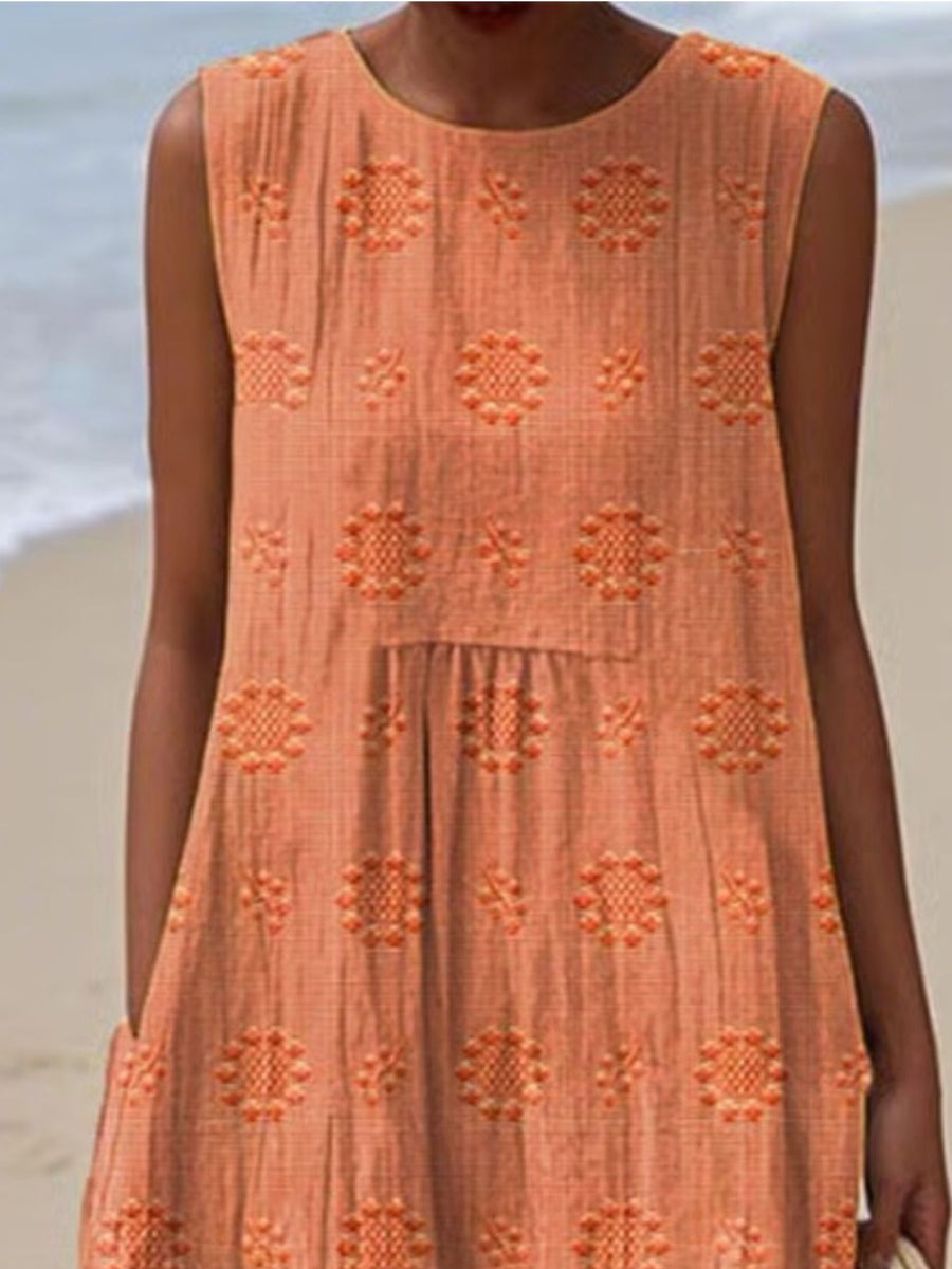 Person wearing an orange dress with floral patterns on a beach.
