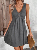 Woman wearing a gray sleeveless dress against a wooden and concrete wall.