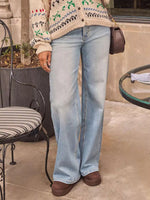 Person wearing light blue jeans and a patterned cardigan in an outdoor setting.