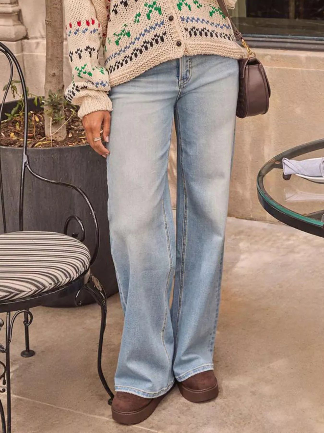 Person wearing light blue jeans and a patterned cardigan in an outdoor setting.