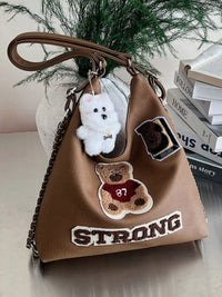 Brown handbag with teddy bear and 'STRONG' patch, white dog keychain, and books in the background