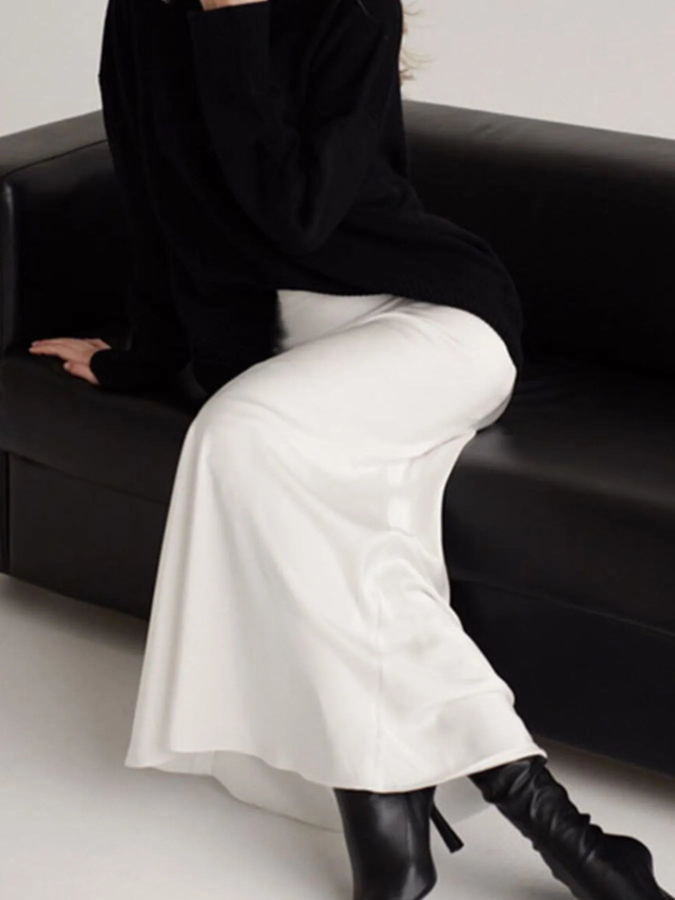 Person wearing a black outfit with white pants and black boots sitting on a black couch.