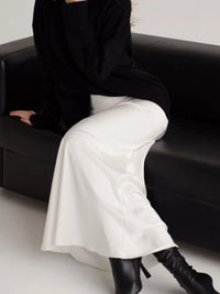 Person wearing a black outfit with white pants and black boots sitting on a black couch.